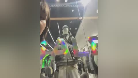 Media: Video of a dark-haired woman wearing a black jacket and a military-style helmet, standing in front of a display of a soldier's mannequin in a futuristic, brightly lit room with colorful lights and a sign reading \"Nakayama Gallery.\