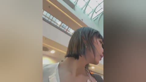 Media: A video of a young woman with short, dark hair, wearing a white shirt, standing in a modern, brightly lit indoor space with glass ceilings and large windows.