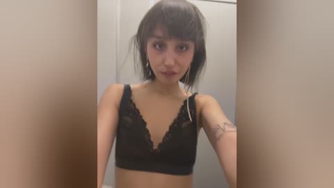 Media: Video of a young Asian woman with straight black hair, wearing a black lace bralette, standing in a narrow, beige-tiled hallway.