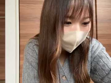 Media: Video of a young Asian woman with long, straight brown hair, wearing a gray cardigan and beige face mask, indoors with wooden paneling background.