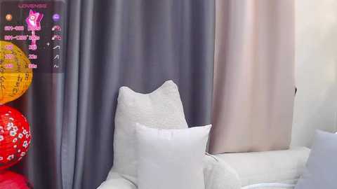 Media: Video of a modern living room with a white sofa and pillows, gray and beige curtains, and colorful paper lanterns on the left.