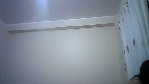 Media: Video of a dimly lit, sparsely furnished room with white walls, a white ceiling, and a small, white window with light coming through. The room has a minimalist design, with no visible furniture or decorations.