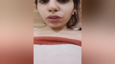 Media: A video of a young woman with light brown skin and dark hair, wearing a white towel with a red band, taken in a bathroom with beige tiles.