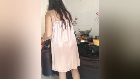 Media: A video shows a woman with long black hair, wearing a light pink, sheer nightgown, standing in a kitchen. She holds a black suitcase, and the kitchen is cluttered with cooking utensils and food items.