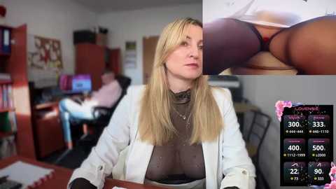 Media: Video of a blonde, fair-skinned woman in a white lab coat, sitting at a desk in an office, with a close-up inset of her underwear-clad buttocks.