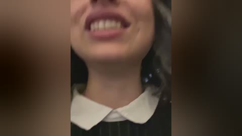 Media: Video of a smiling woman with fair skin, dark hair, and a white collared shirt, viewed from the neck up.