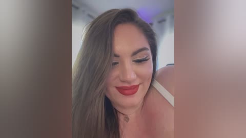 Media: Video of a smiling woman with long brown hair, wearing red lipstick and white lingerie, captured from a low angle.