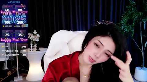 Media: Video of an Asian woman with long black hair in a red satin robe, lying on a bed, with a digital screen displaying festive dates in the background.