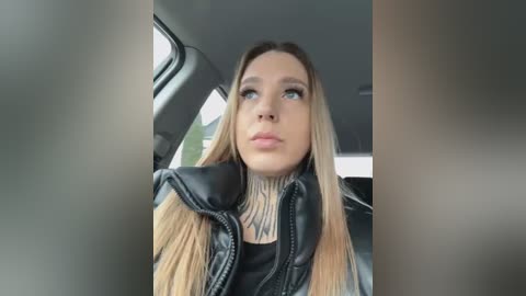 Media: Video of a young woman with long, blonde hair, wearing a black leather jacket, inside a car, looking thoughtful.