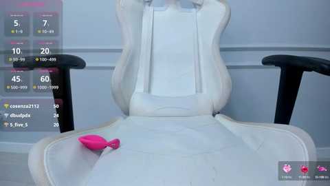 Media: Video of a white gaming chair with a pink vibrator on its armrest in a minimalist room, with a digital display showing various metrics in the background.