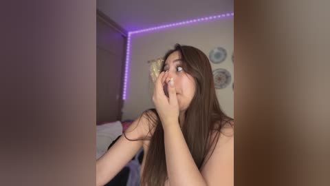 Media: Video of a young woman with long brown hair, looking surprised, in a dimly lit bedroom with purple LED strip lighting on the ceiling.