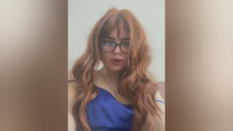 Media: Video of a woman with long, wavy auburn hair, wearing black-rimmed glasses, and a blue and white outfit, blurred in the middle.