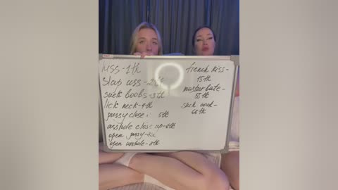 Media: A video featuring two women in lingerie, holding a whiteboard with explicit sexual instructions. The background is dark, with a blurred curtain.