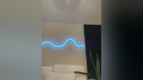 Media: Video of a minimalist living room with a white couch and a vibrant blue neon wave light on a beige wall. A tall, green plant is visible in the right corner.