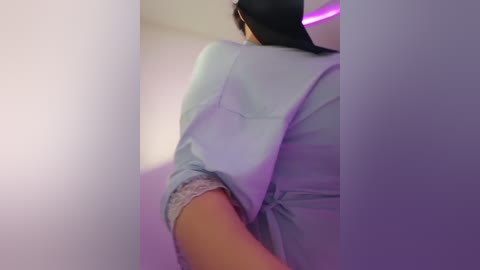 Media: A video of a person's upper body, wearing a light blue shirt, partially visible, with a black headband, in a dimly lit room with purple lighting.