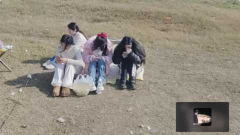 Media: Video of four women in white robes and headscarves, sitting on the ground in a barren, grassy field, looking distressed. A small inset shows a woman in black, crying.