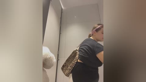 Media: A video shows a woman with a leopard print handbag and pink hair, partially obscured by a white, fluffy object, likely a stuffed toy. The background features a sleek, modern interior with gray walls and a tiled floor.