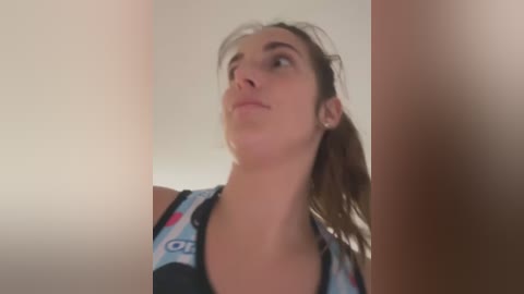 Media: A video of a young woman with fair skin and light brown hair, wearing a colorful, patterned tank top, looking upward with a contemplative expression.