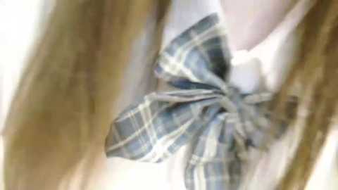 Media: A close-up video of a young girl wearing a plaid school uniform with a large, bow-tied necktie. Her long, light brown hair falls over her shoulders. The background is blurred, focusing attention on the uniform details.