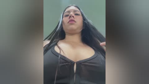 Media: A video of a plus-size woman with long black hair, wearing a low-cut black top, and a necklace, with a blurred background.