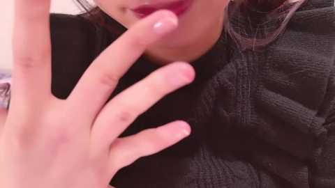 Media: Close-up video of a woman with light skin, wearing dark lipstick, touching her lips with her right hand, wearing a dark sweater.