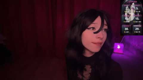 Media: A dimly-lit video of a young woman with long black hair and pale skin, wearing a black outfit, standing in a room with red curtains and purple lighting. A digital screen in the background displays a virtual reality interface.