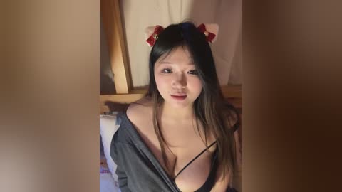 Media: Video of an East Asian woman with long black hair and fair skin, wearing a black bra and open grey robe, in a dimly lit bedroom with wooden furniture.