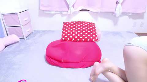 Media: Video of a child lying on a bed with a pink blanket and a red polka-dotted pillow, surrounded by pastel-colored drawers and hanging clothes.