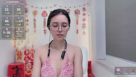 Media: A video of an Asian woman with fair skin, glasses, and a pink lace dress, standing in a room adorned with Chinese New Year decorations.