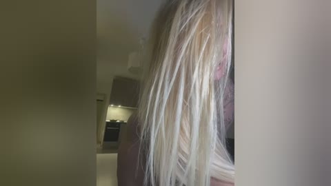 Media: Video of a woman with long, platinum blonde hair, partially cropped, standing in a modern kitchen with beige walls and stainless steel appliances.