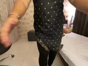 Media: A video of a person in a black, polka-dotted mini-dress with gold fringe, standing in a bedroom with white tiled floors, a bed, and patterned wallpaper.