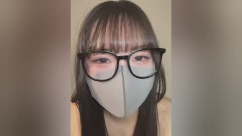 Media: Video of an Asian woman with long dark hair, wearing black-rimmed glasses and a light blue face mask, against a plain beige background.