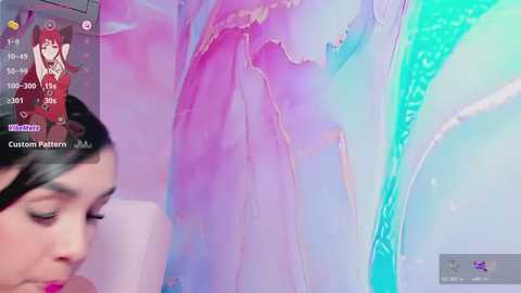 Media: Video of a woman with long red hair, wearing a pink dress, standing in a room with colorful, abstract, pastel-colored walls and a blue-green curtain.