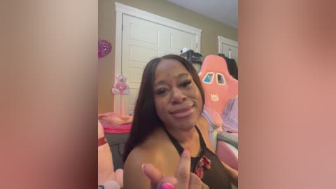 Media: A video of a young Black woman with long, straight black hair and a playful expression, wearing a black tank top, surrounded by colorful, plush toys in a cluttered bedroom.