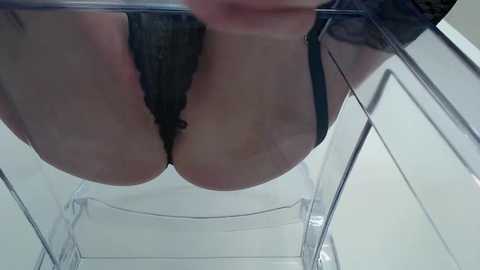 Media: A low-angle video shows a woman's ample breasts in a black lace bra, partially obscured by a clear plastic container, creating a distorted, reflective view.