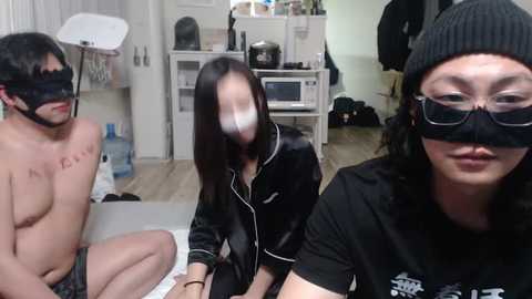 Media: Video of two Asian women and a man in a domestic setting, all wearing black masks, one man shirtless.