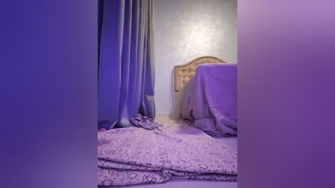 Media: A video of a dimly lit bedroom with lavender curtains, a wooden headboard, and a bed covered in a lavender and white floral sheet. The floor is covered in a similar patterned rug. The ambiance is serene and cozy.