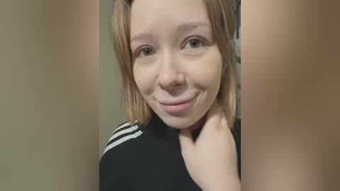 Media: A close-up video of a young Caucasian woman with fair skin, straight brown hair, and green eyes. She has a slight smile and is wearing a black top with white stripes.