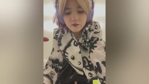 Media: Video of a young Asian woman with fair skin, short blonde hair, wearing purple headphones and a black-and-white patterned coat, seated in a dimly lit indoor setting, possibly a subway.