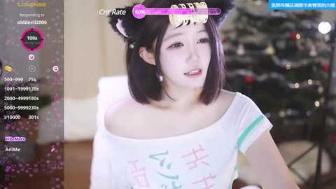 Media: Video of an Asian woman with pale skin, short black hair, wearing a white t-shirt with a cartoon character, sitting indoors near a Christmas tree.