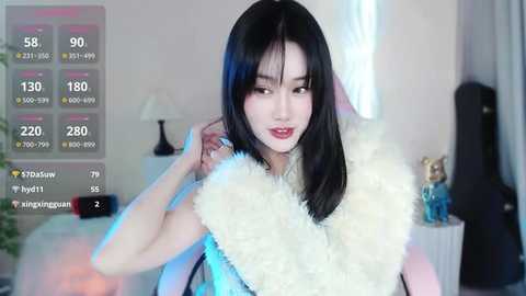 Media: Video of a fair-skinned, slender East Asian woman with long black hair, wearing a white fur coat, in a modern, softly lit room with a digital weather overlay.