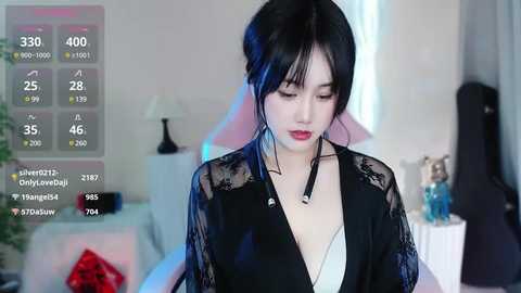 Media: A video of a young East Asian woman with fair skin and long black hair, wearing a black lace robe, standing in a modern bedroom.