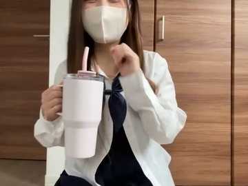 Media: Video of an Asian woman with long brown hair, wearing a white face mask and blue shirt, holding a pink insulated mug with straw, against wooden cabinet background.