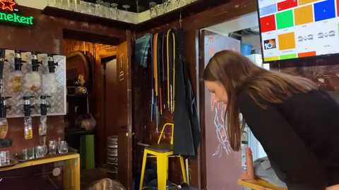 Media: Video of a cozy, rustic bar with wooden walls, hanging beer taps, colorful posters, and a woman in a black top leaning on a counter.