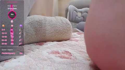 Media: A video of a woman's foot in a cozy, gray, quilted slipper on a pink, floral-patterned blanket. The background shows a gray, tufted headboard.