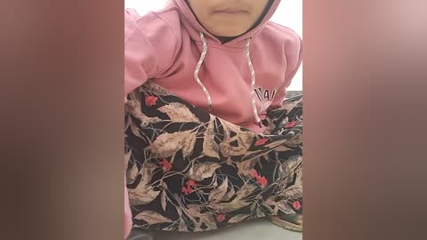 Media: A video of a person wearing a pink hoodie with a floral skirt featuring red and beige patterns. The person's face is partially visible, but not fully.