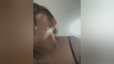 Media: Video of a young woman with wet, curly brown hair, partially blurred, wearing a black bra. She has light skin and is seen from the side.