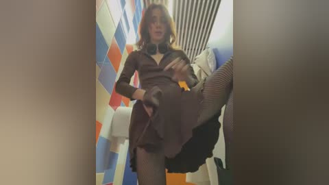 Media: A video of a person with shoulder-length blonde hair, dressed in a brown outfit with fishnet stockings, performing a kick in a colorful, tiled bathroom.