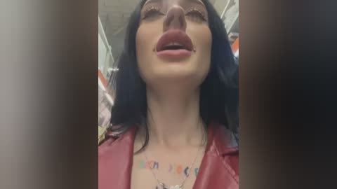 Media: Video of a woman with long black hair, wearing a red leather jacket, and a colorful necklace, captured from a low angle, showing her open mouth and slightly closed eyes.