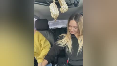 Media: Video of a car interior showing a woman with long blonde hair, wearing a black jacket, and a man in a yellow sweater, both seated. A large, white, moldy object hangs from the ceiling.